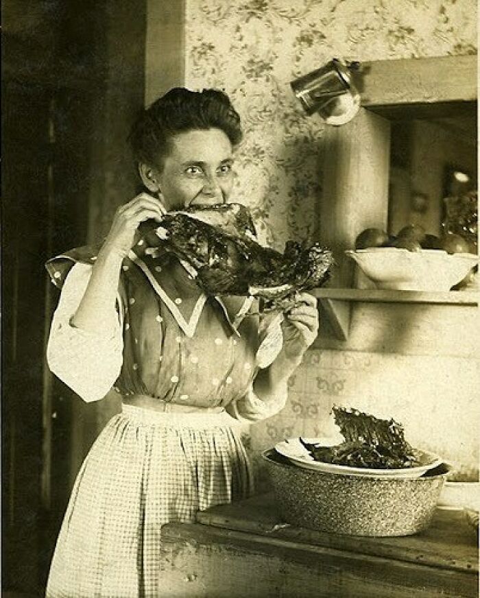 Vintage black and white photo of a woman in old-fashioned clothing eating a large piece of meat, odd and creepy scene.