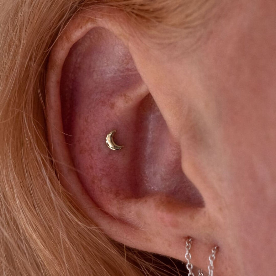 Close-up of ear with moon-shaped cartilage piercing and chain earrings showcasing different types of ear piercing styles.