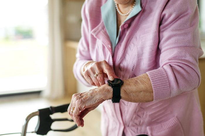 Elderly woman in pink sweater using a smart watch, highlighting SOS technology in modern rescue missions.