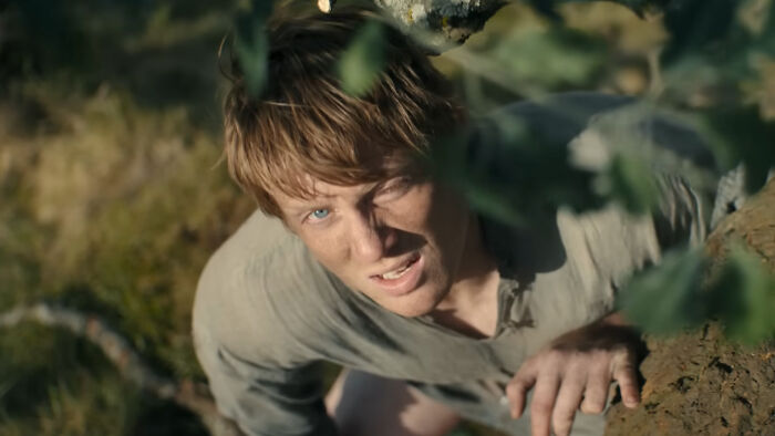 Young man climbing a tree in a forest scene from A Knight of the Seven Kingdoms, related to George RR Martin&rsquo;s work.