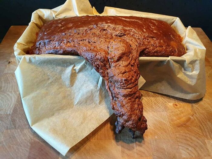 A burnt dessert cake overflowing and misshapen in a parchment-lined loaf pan showing ruined dessert mishap.