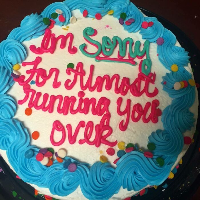 Round cake with blue frosting border and colorful sprinkles, featuring humorous red and green icing text apology, funny cake emotions.