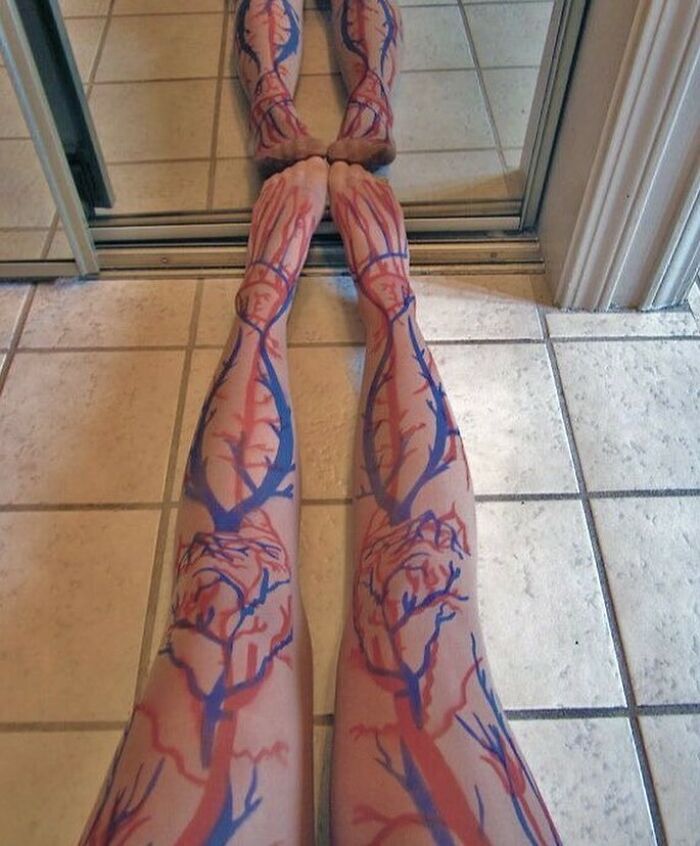 Piernas con pintura anatómica de venas y arterias reflejadas en un espejo, imagen médica extraña y fascinante.