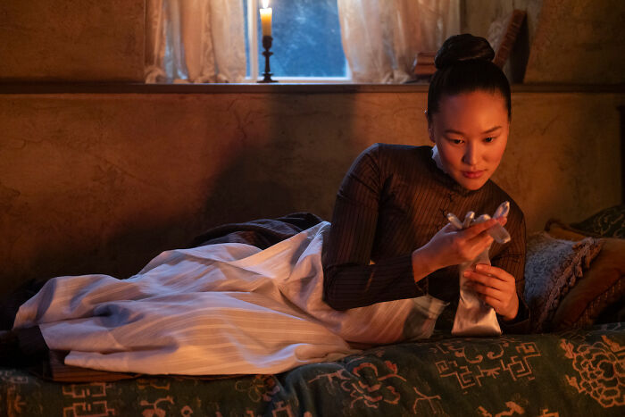 Actress from Bridgerton Season 4 cast list reclining on a vintage bed in period costume by candlelight.