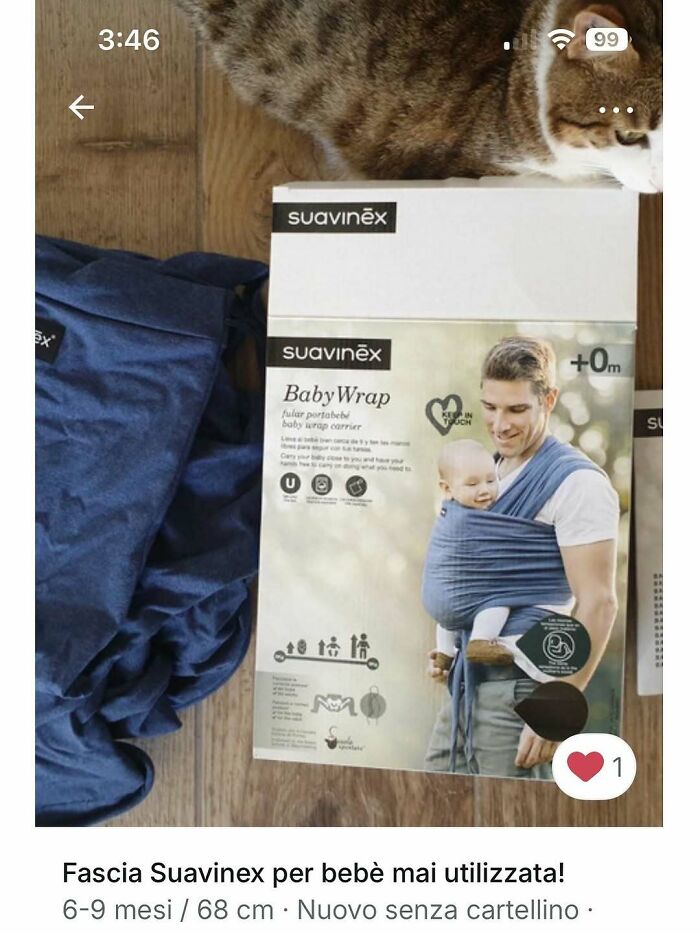Cat walking on wooden floor beside baby wrap packaging showing a man carrying a baby in a blue cloth wrap.