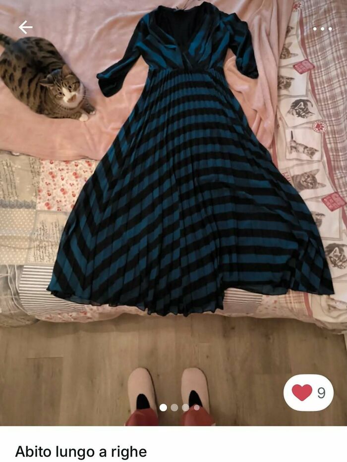 Cat lying on bed next to a black and blue striped dress, highlighting cats stealing the spotlight in Vinted ads.
