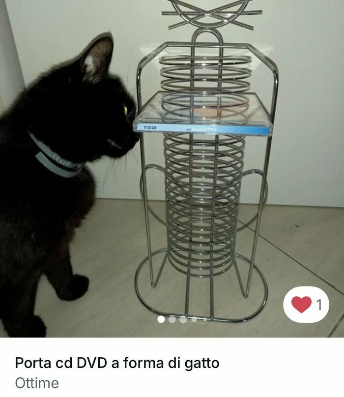 Black cat curiously inspecting a cat-shaped metal DVD holder, highlighting cats stealing the spotlight in ads.