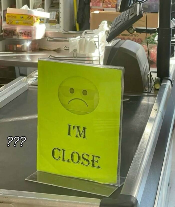 Yellow sign with a sad face emoji and the words "I'M CLOSE" on a store counter, a bizarre meme confusing shoppers.