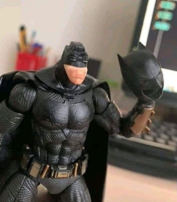 Batman action figure with a bizarre face holding its own mask in a random and bizarre meme style image.