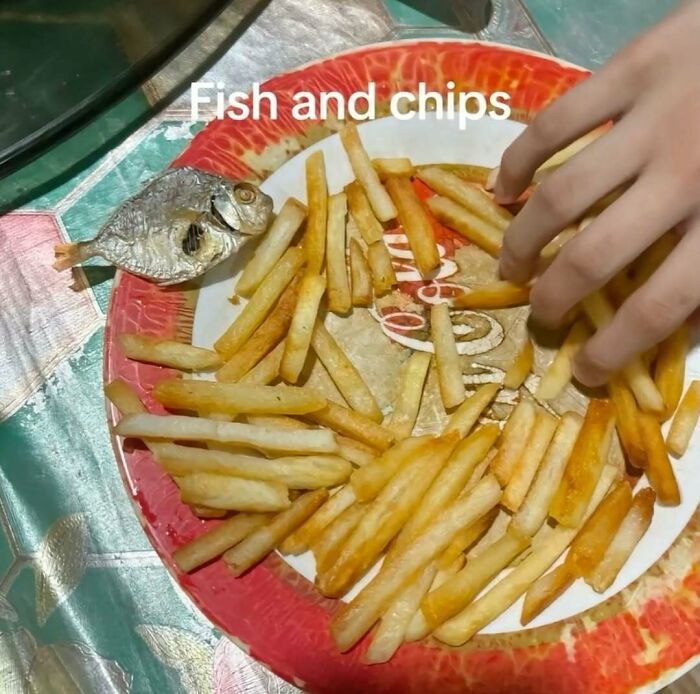 A small dried fish with fries on a red plate, captioned with fish and chips, depicting a bizarre meme.
