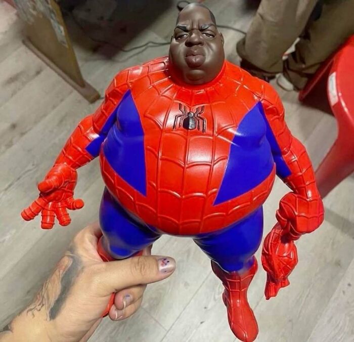 Hand holding a bizarre Spider-Man figure with an exaggerated, overweight body as a random meme toy.