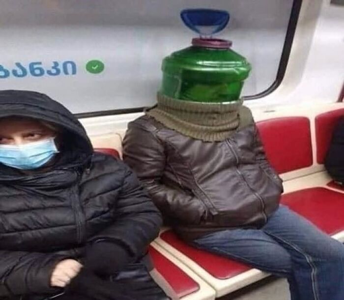 Person wearing a large water jug on their head sitting next to a masked passenger on public transport, random and bizarre meme.