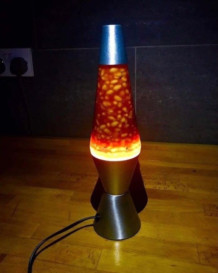 Lava lamp filled with baked beans on a wooden surface, creating a bizarre and random visual effect.