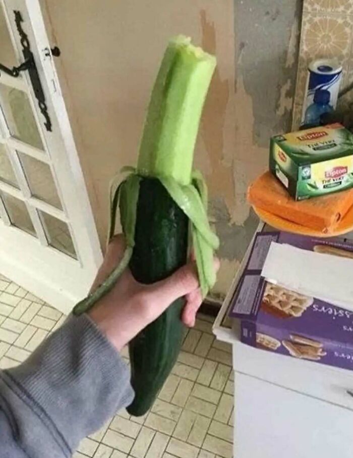 Hand holding a peeled cucumber resembling a banana in a kitchen, one of the random and bizarre memes.