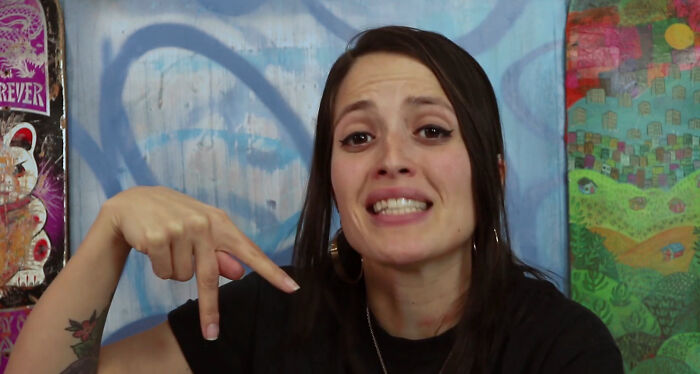 Woman with dark hair and hoop earrings pointing downward, featured in The Pitt Season 2 guest star discussion.