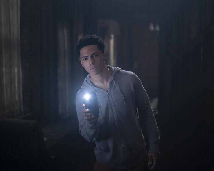 Young man in a hoodie shining a flashlight in a dark room from The Pitt season 2 guest star episode 3.