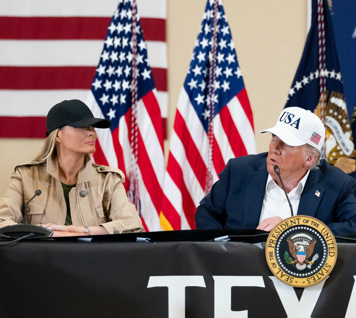 Melania Trump and Donald Trump at Mar-a-Lago event with USA hats and American flags in the background, showing body language.