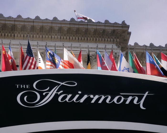 Entrance sign of the Fairmont hotel in San Francisco with various international flags displayed above the building facade.