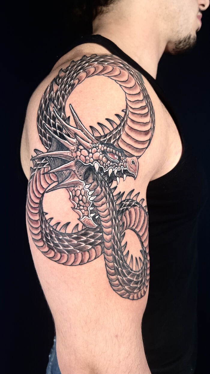 Tattoo of a detailed dragon with scales and horns on a man's upper arm, showcasing cool tattoo design skills.