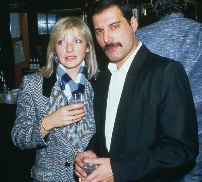 Freddie Mercury with a woman at a social event, both holding drinks, highlighting Freddie Mercury's secret daughter story.