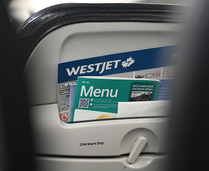 Sardine can seating close-up of WestJet seat pocket with menu in cramped airplane cabin