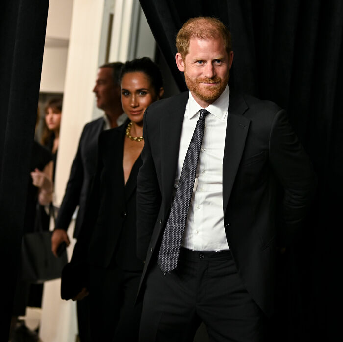 Prince Harry and Meghan Markle in formal attire at an event, with a blurred crowd in the background.