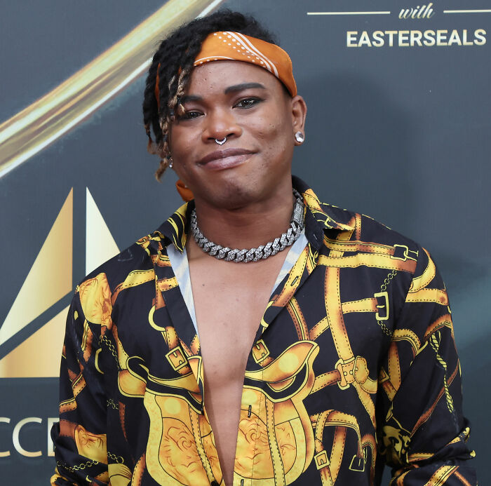 Person wearing an open patterned shirt and orange headband at an event related to Will Smith accused of harassing musician.