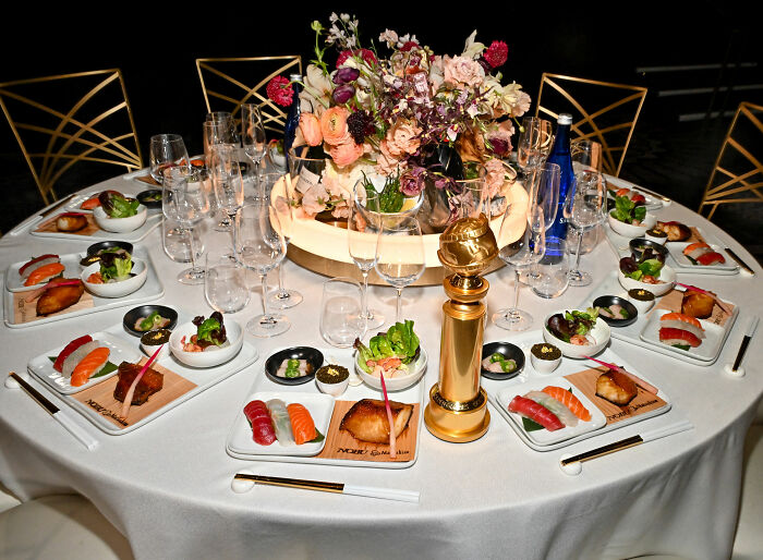 Golden Globes food presentation with sushi plates, salads, a gold trophy centerpiece, and floral arrangement on a round table. Golden Globes food presentation with sushi plates, salads, a gold trophy centerpiece, and floral arrangement on a round table.