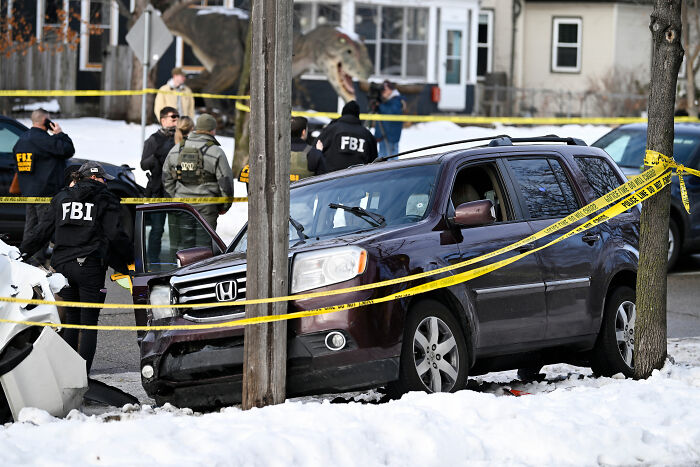 FBI agents examine a crime scene with a crashed SUV and police tape after an incident involving an ICE agent and a slain mom.
