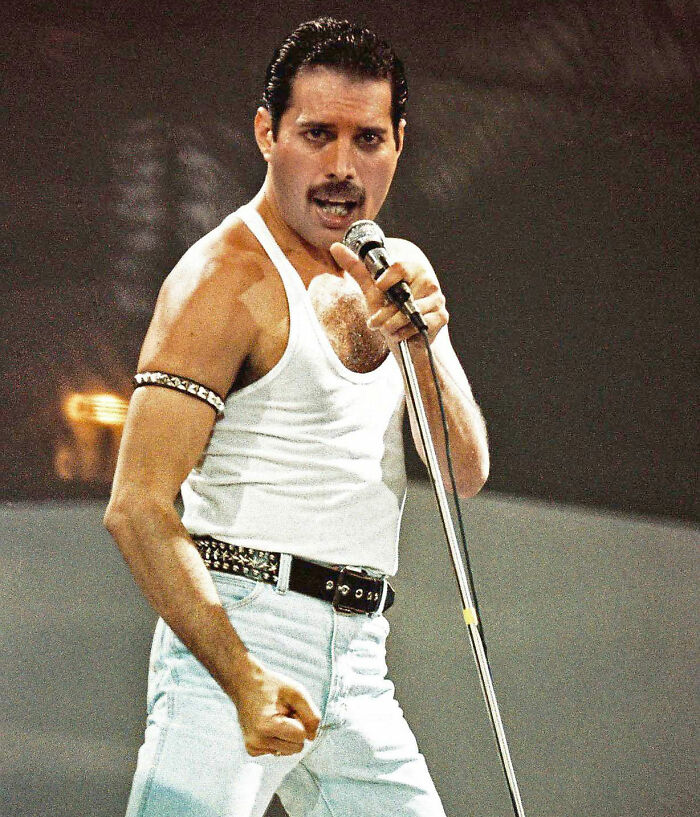 Freddie Mercury performing on stage in a white tank top and jeans, highlighting news of his secret daughter passing away.