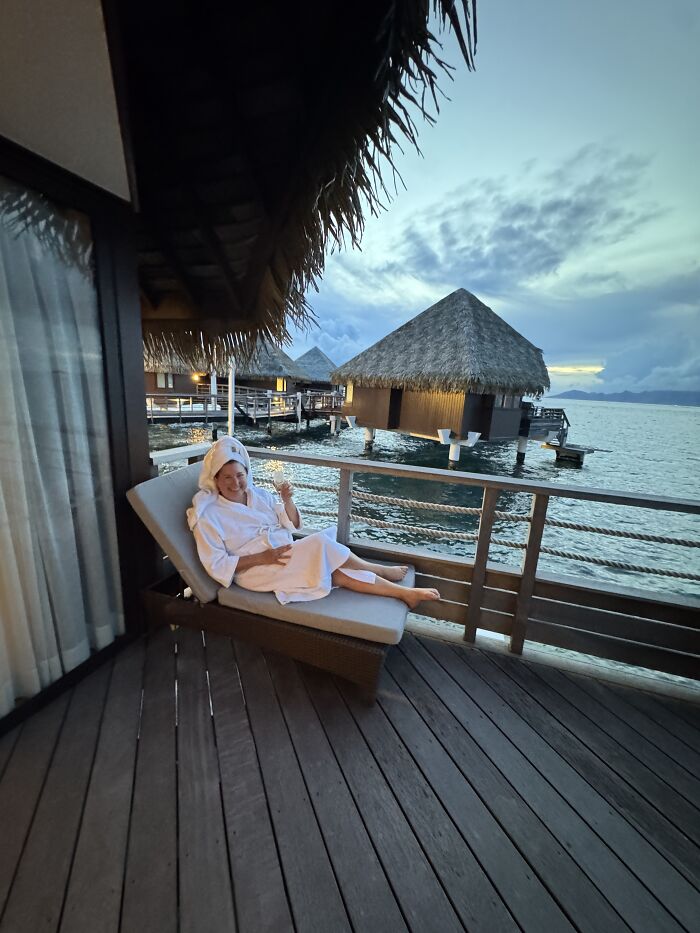 Woman relaxing on a deck chair at a French Polynesia overwater bungalow resort with vibrant shades of blue sky and sea.