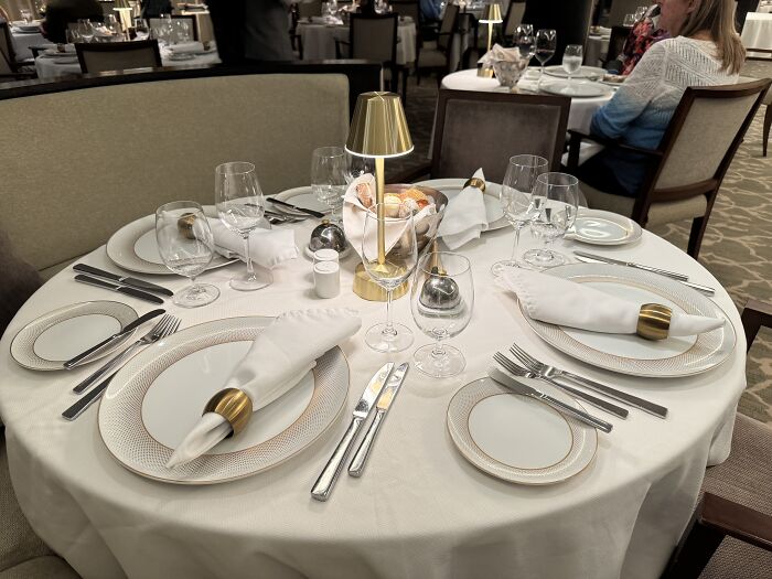 Elegant dining table setting with white linen, gold-accented plates and napkins, ready for a French Polynesia sailing experience.