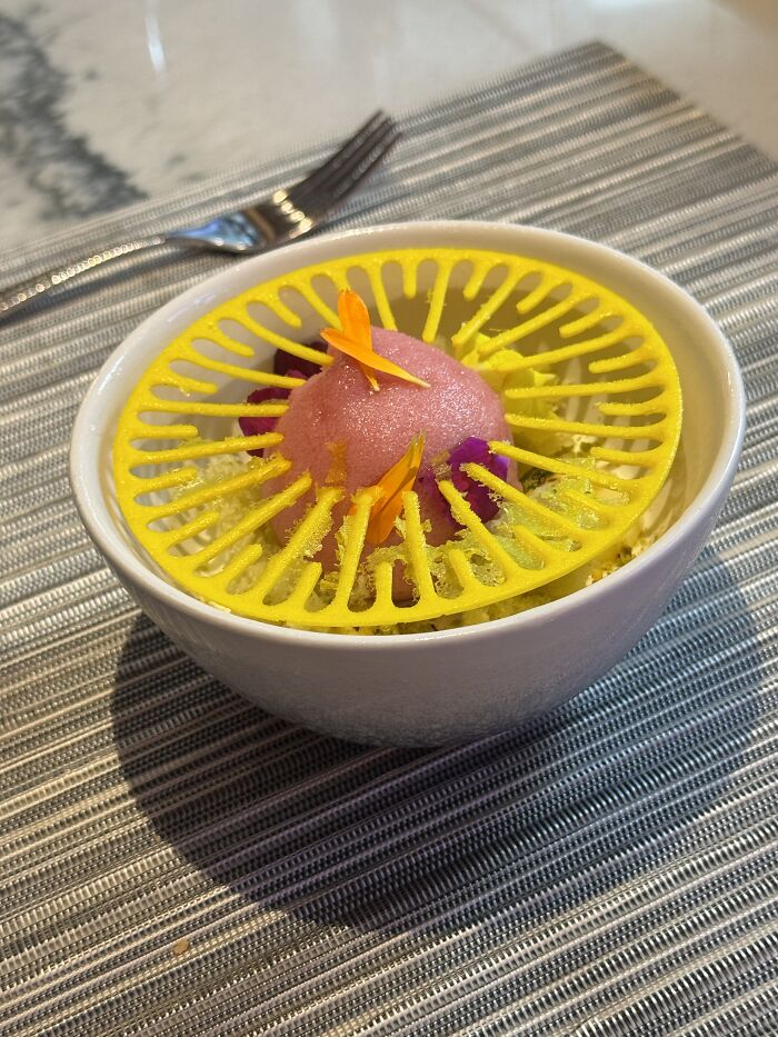 Pink sorbet dessert in a white bowl with yellow decorative topping on a striped tablecloth, French Polynesia inspired.