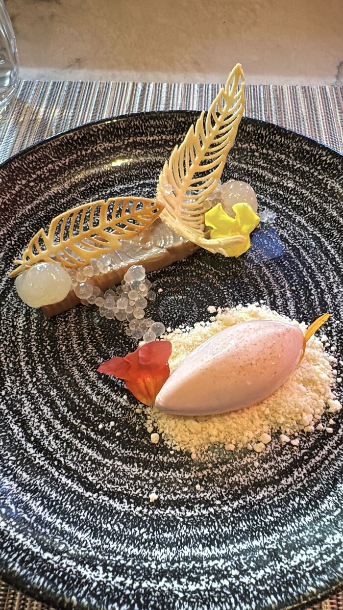 Elegant dessert plated with intricate leaf-shaped decorations and fruit pearls, showcasing shades inspired by French Polynesia blue.