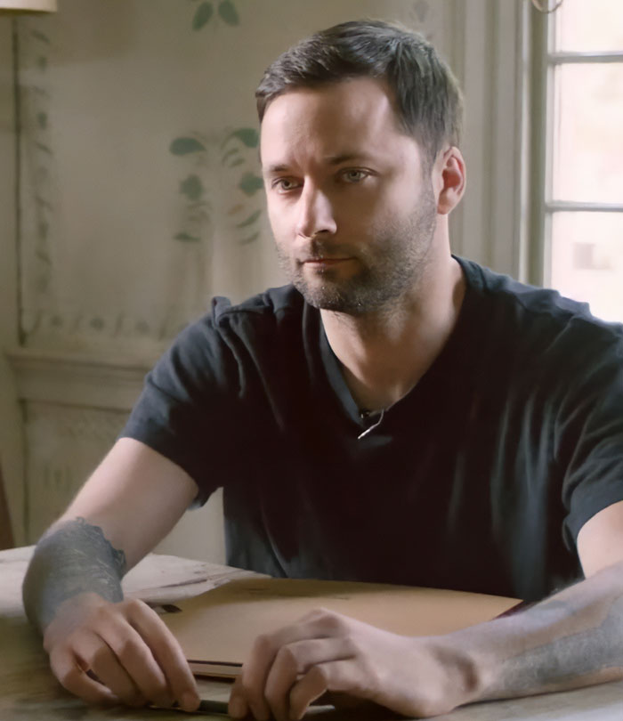 Man with a serious expression sitting at a table indoors, related to disturbing new details after violent crime arrest in Hollywood.