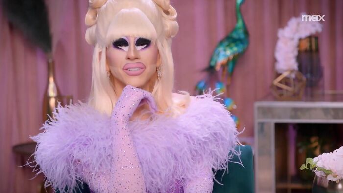 Drag performer in a glamorous lavender feathered outfit, showcasing celebrities who weren't nepo babies and achieved success independently.