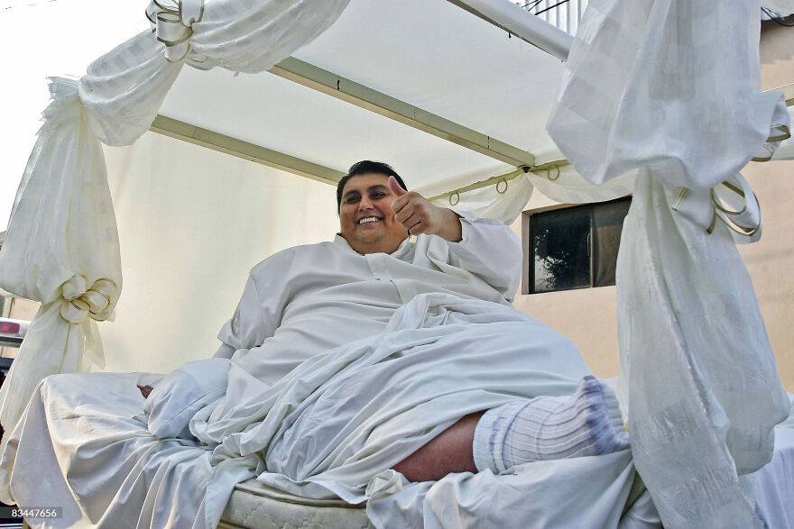A heaviest recorded person Manuel Uribe in history giving a thumbs up while lying on a covered outdoor bed.