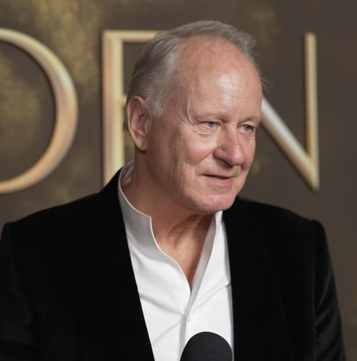 Stellan Skarsg&aring;rd speaking at an event, wearing a white shirt and black jacket, addressing Critics Choice Awards food criticism.