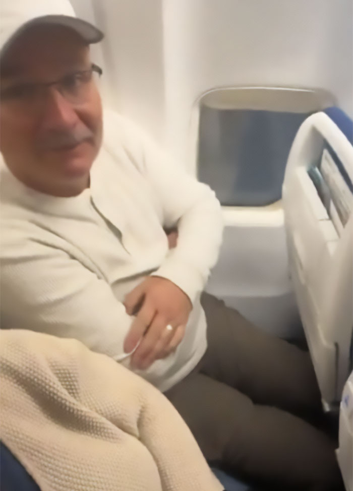 Man in cramped airplane seat showing sardine can seating with limited legroom by window