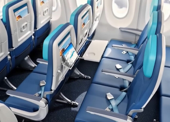 sardine can seating on new plane, cramped blue seats with narrow legroom, tray tables down and small seatback screens visible