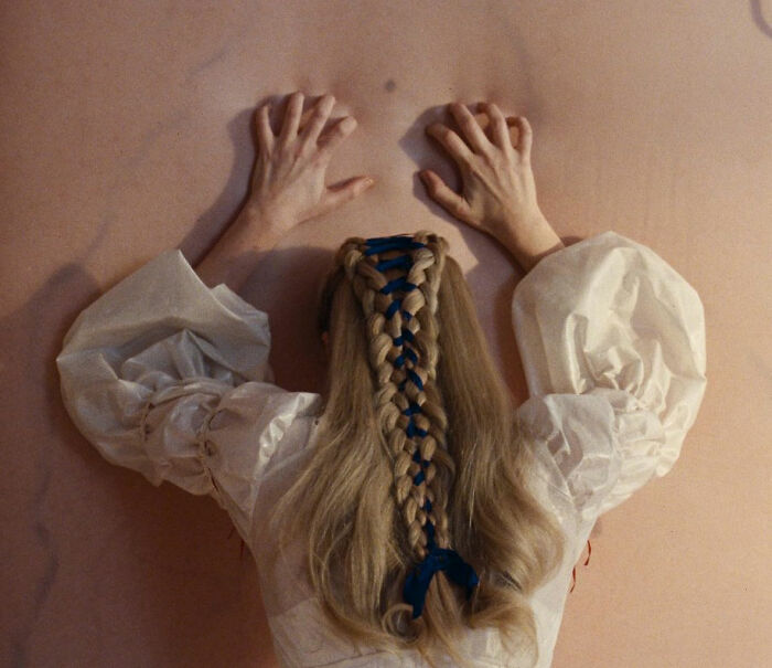 Woman with braided hair tied with blue ribbon wearing a white blouse, evoking Margot Robbie on-set relationship with Wuthering Heights co-star.