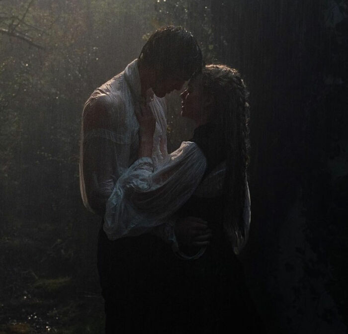 Couple embracing in dim forest light, woman wearing a bathing suit with sleeves in a romantic movie scene.