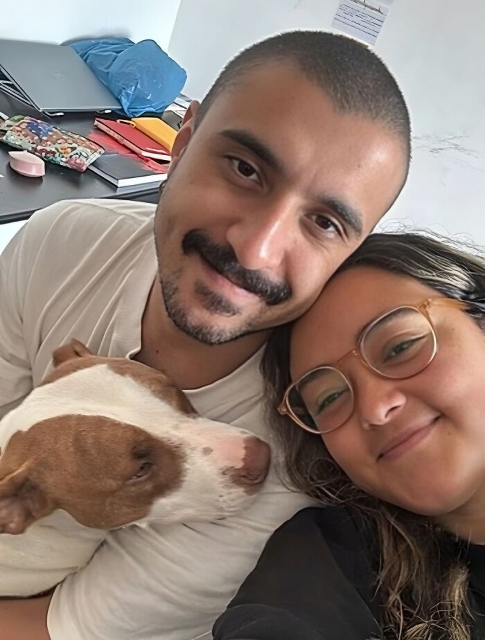 Man and woman smiling with a rescued pit bull, showing a pit bull going from scared to spoiled in a loving home.