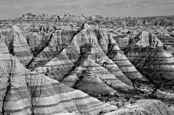 Black and white photo of layered rock formations in a rugged landscape showcasing natural patterns and textures.