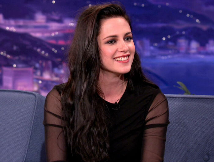 Young female celebrity with long dark hair smiling during a television interview about celebrity downfall stories.