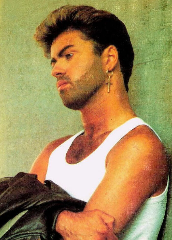 Man with beard and cross earring in a white tank top, appearing contemplative, related to celebrity downfalls theme.