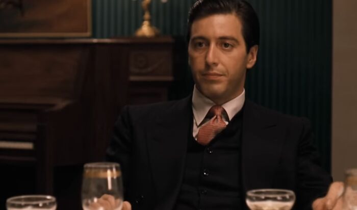 A man in a black suit and red tie sitting at a table with drinks, representing famous villains including Lord Voldemort pure evil.