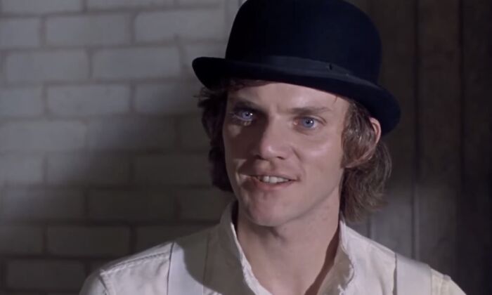 Young man with blue eyes wearing a black bowler hat and white shirt, representing a famous villain in a dimly lit room.