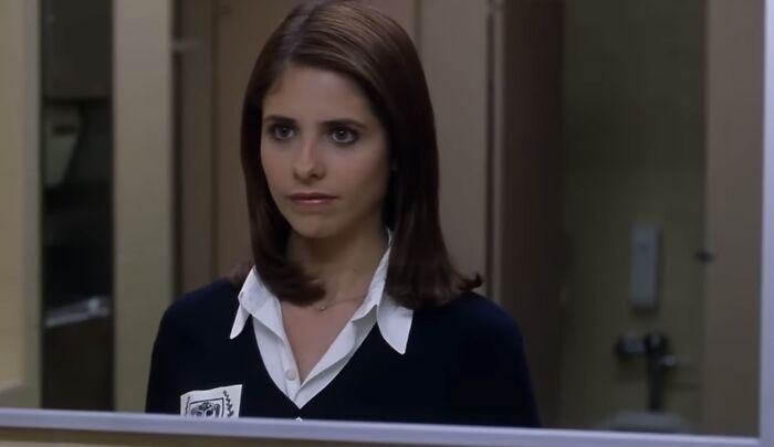 Young woman with dark hair in school uniform, looking thoughtfully into a mirror, exploring the concept of pure evil villains.