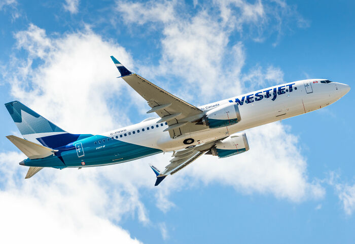 WestJet airplane in flight against blue sky, highlighting sardine can seating on new planes